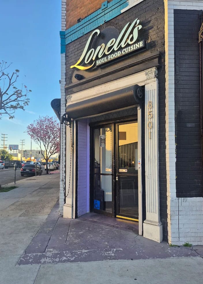 Exterior storefront of Lonell's Soul Food Cuisine at 8501, featuring a black brick facade, white pillars, and a glowing golden sign above a glass double-door entrance